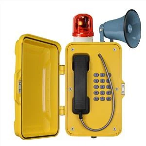Yellow weatherproof industrial telephone mounted on a wall with a sturdy handset and keypad designed for harsh outdoor environments. The background shows an industrial setting with metal structures and safety signage. The scene conveys reliability and safety in challenging conditions.